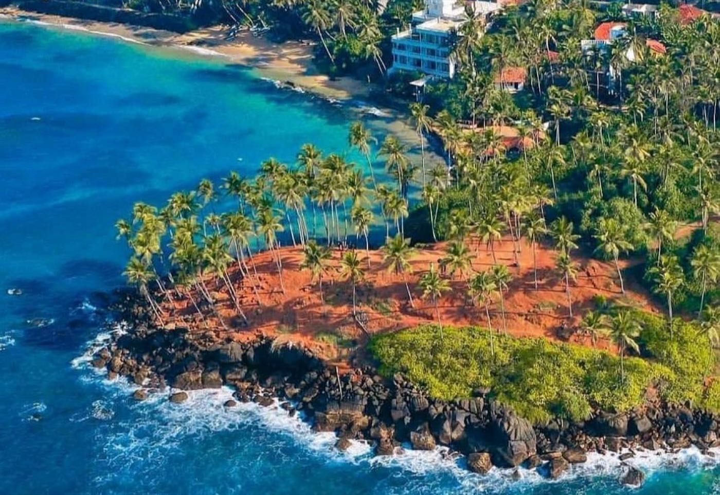 The palm-covered headland at Coconut Tree Hill from the air, with Mirissa's bay and turquoise water behind it